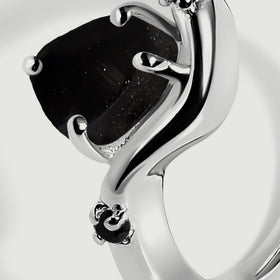 The side of the raw black stone shows an uneven surface beside polished silver and a small black accent.