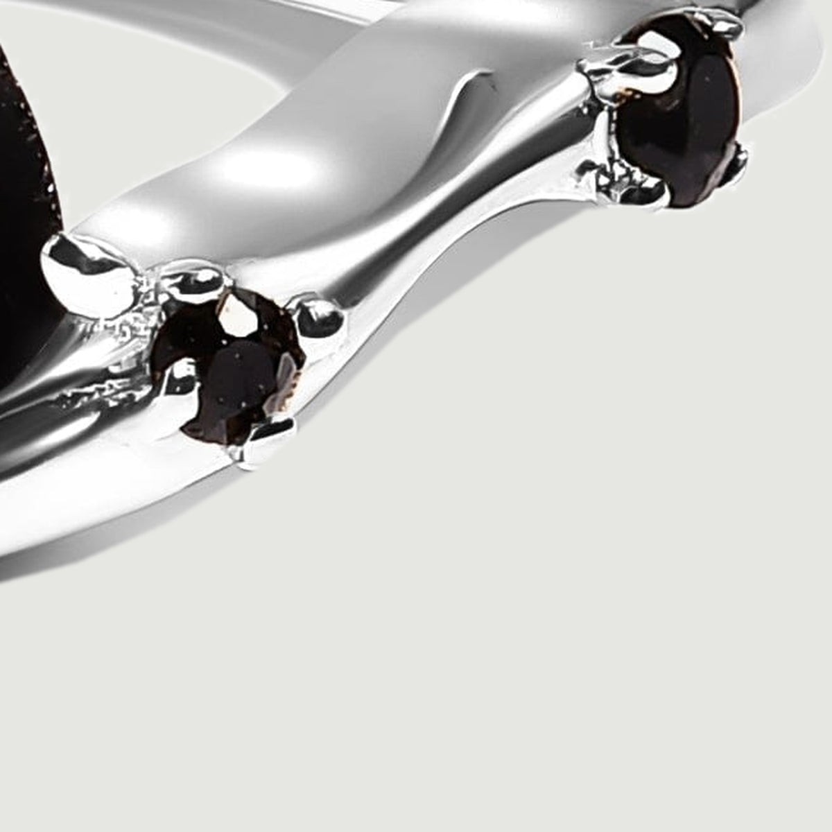 Two small black stones sit in silver claw settings along the curved right shoulder of the ring.