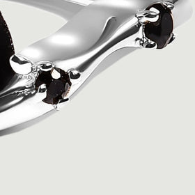 Two small black stones sit in silver claw settings along the curved right shoulder of the ring.