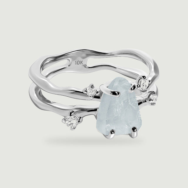 A white gold ring displays a raw aquamarine held by polished prongs beside four clear accent stones.