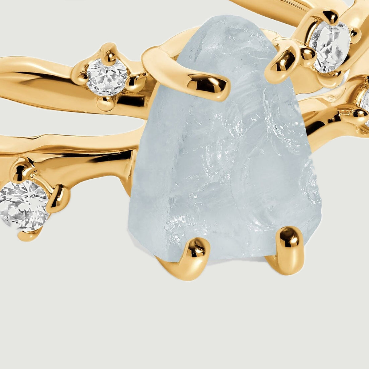 A close view shows the uneven aquamarine surface and yellow gold prongs beside clear round accent stones.