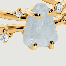 A close view shows the uneven aquamarine surface and yellow gold prongs beside clear round accent stones.