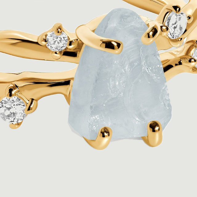 A close view shows the uneven aquamarine surface and yellow gold prongs beside clear round accent stones.