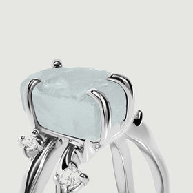 The rough blue crystal rises above white gold prongs with two small clear stones below the setting.
