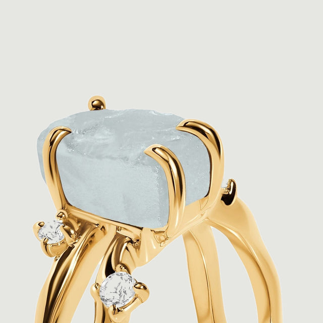 Yellow gold prongs curve around the raw blue aquamarine above two separated ring bands.
