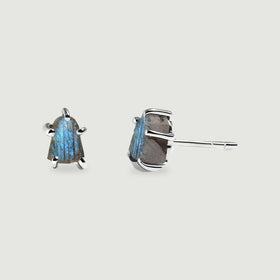 Two raw labradorite studs in silver-colored prong settings show a blue stone face and a straight post on a light gray surface.