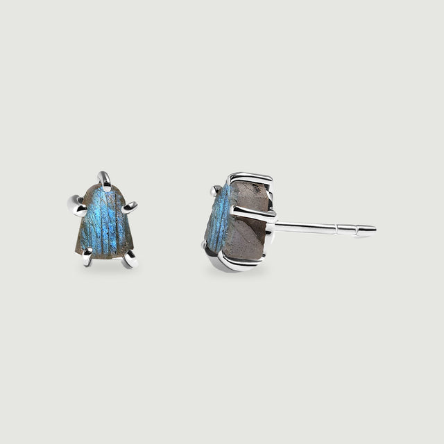 Two raw labradorite studs in silver-colored prong settings show a blue stone face and a straight post on a light gray surface.