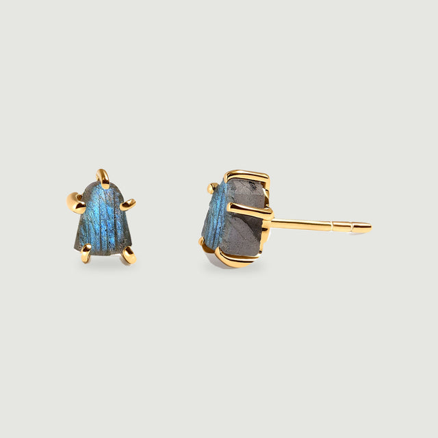 A pair of yellow gold-colored labradorite studs displays rough blue-gray stones and an exposed post against a pale gray background.