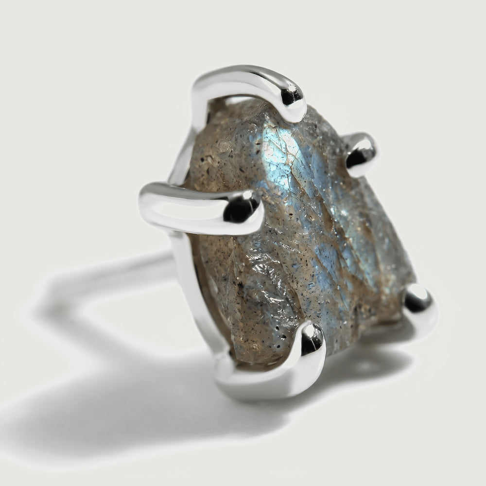 A close view shows the raw gray labradorite surface, a pale blue flash, and rounded silver-colored prong tips.