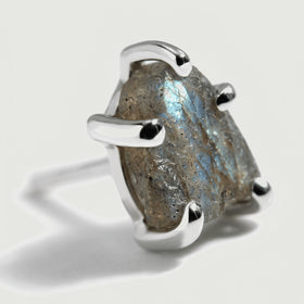 A close view shows the raw gray labradorite surface, a pale blue flash, and rounded silver-colored prong tips.
