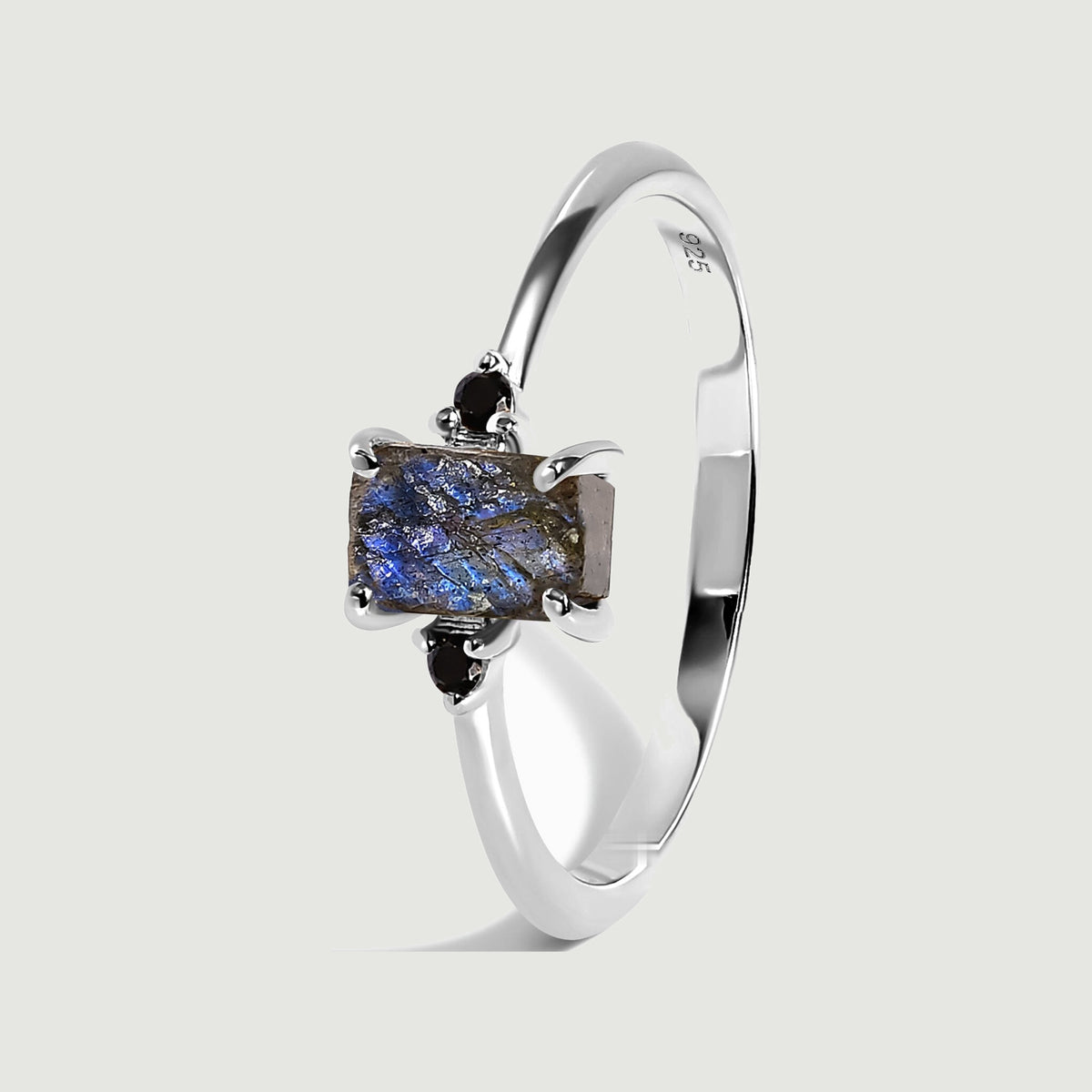 The sterling silver ring stands at an angle, showing the rough blue stone, black side stones, and polished band.