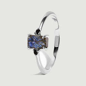 The sterling silver ring stands at an angle, showing the rough blue stone, black side stones, and polished band.