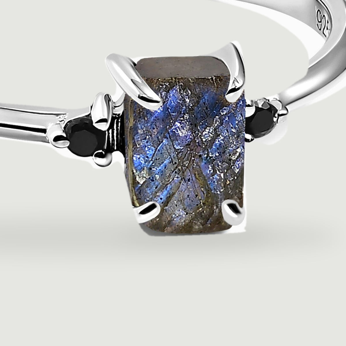 A close view of the silver prongs shows the raw rectangular labradorite flanked by two faceted black stones.