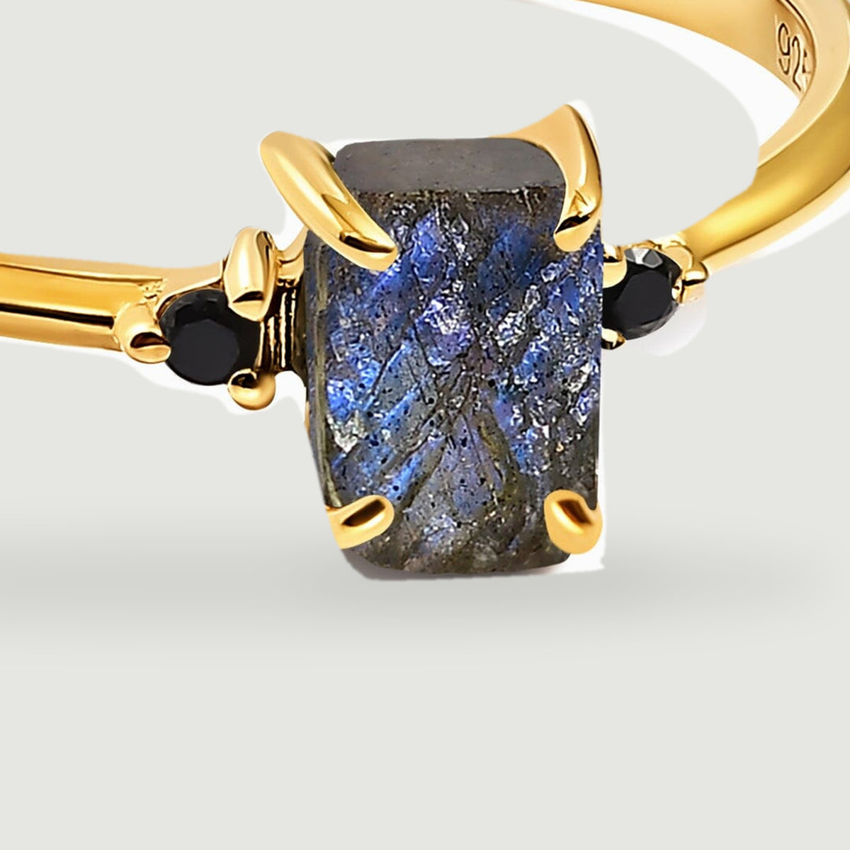 The yellow gold prongs frame a textured blue-grey centre stone between two glossy black accents.