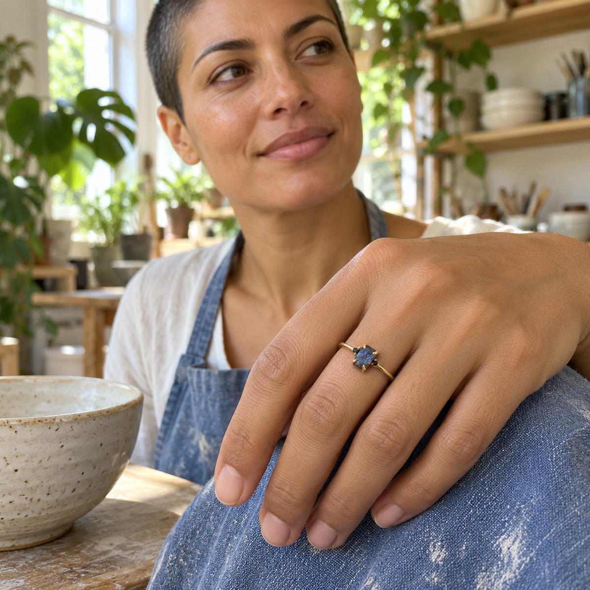 A woman with short dark hair wears the yellow gold vermeil ring with her hand resting against a blue apron in a pottery studio.