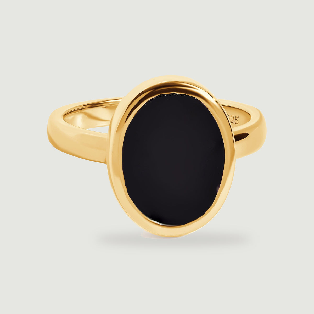 An oval black onyx ring with a polished yellow gold vermeil bezel and band rests on a light grey surface.