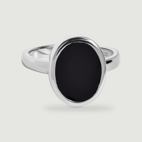 A sterling silver ring with a smooth oval black onyx face is centered above a soft shadow.