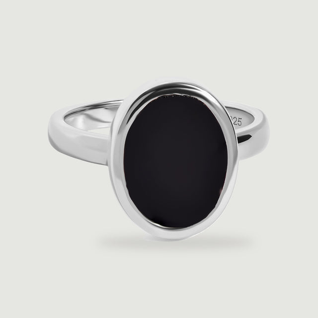 A sterling silver ring with a smooth oval black onyx face is centered above a soft shadow.