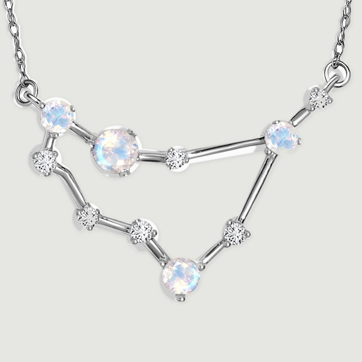 The complete angular pendant rests on a pale gray surface with its two chain attachment loops visible.