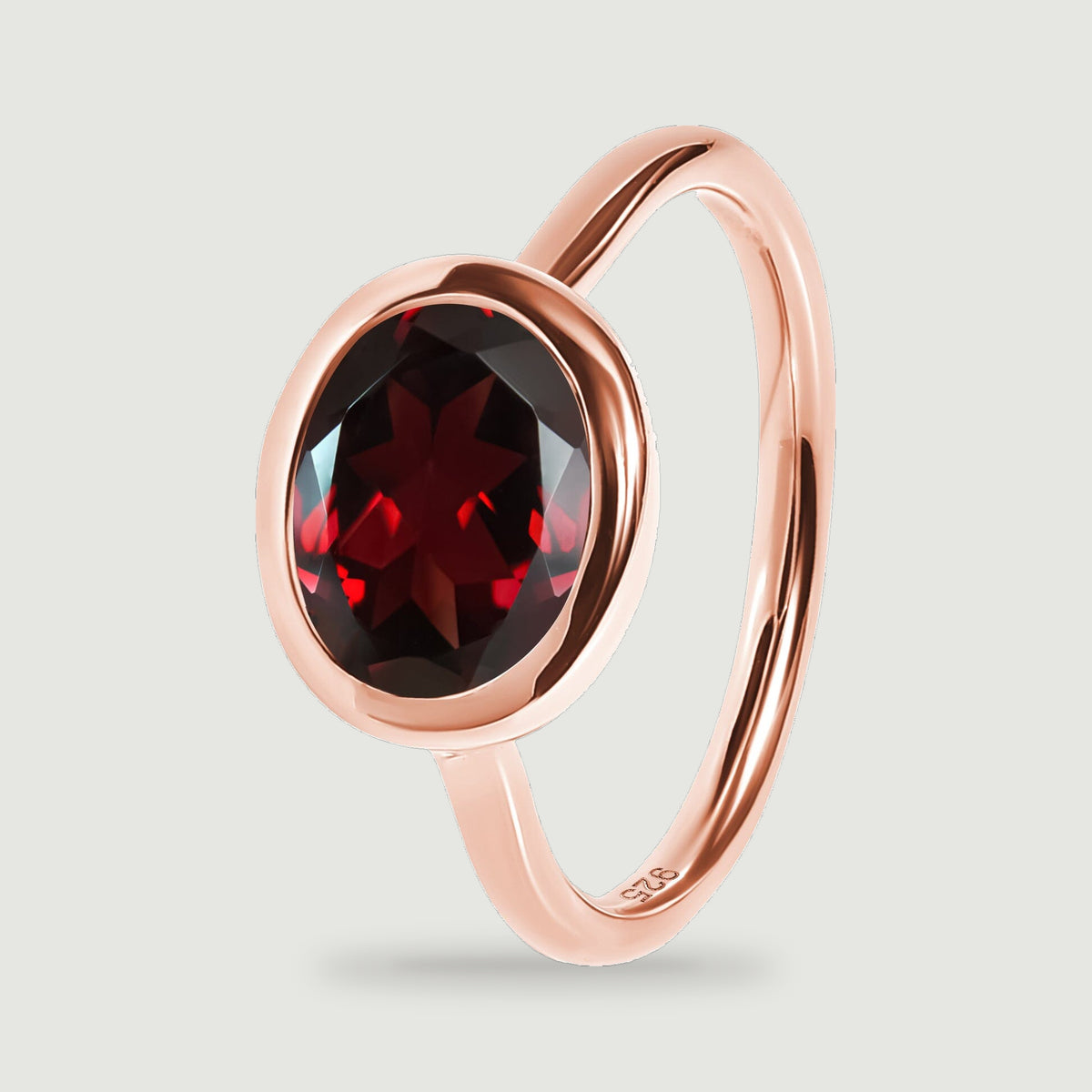 An upright rose gold ring reveals the rounded bezel edge, red stone, and polished band.