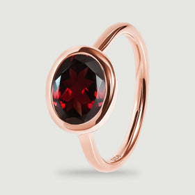 An upright rose gold ring reveals the rounded bezel edge, red stone, and polished band.