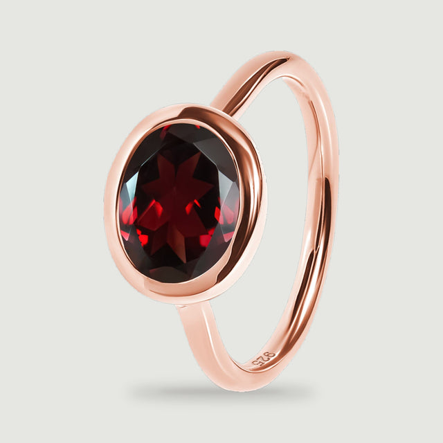 An upright rose gold ring reveals the rounded bezel edge, red stone, and polished band.