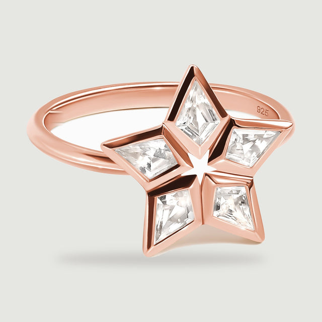 Five clear kite-shaped stones frame an open star on a rose gold ring shown at a low angle.