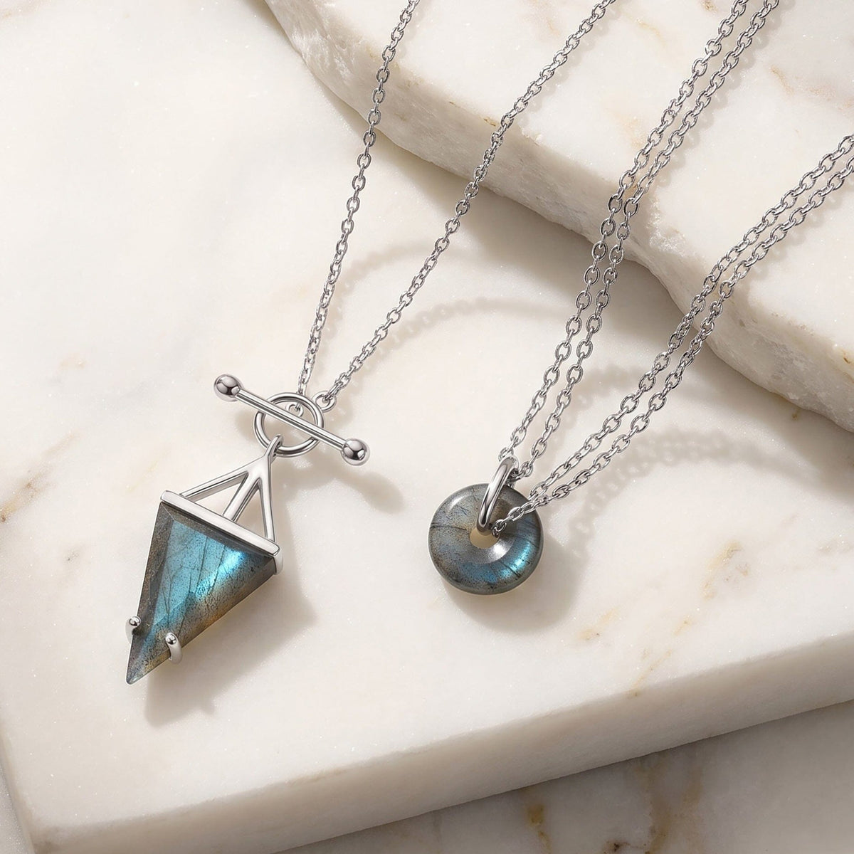 Silver triangle and donut labradorite pendants on a marble surface