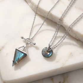 Silver triangle and donut labradorite pendants on a marble surface