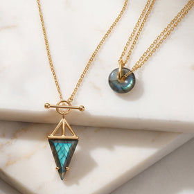 Gold labradorite necklaces with triangle and donut pendants on a marble surface