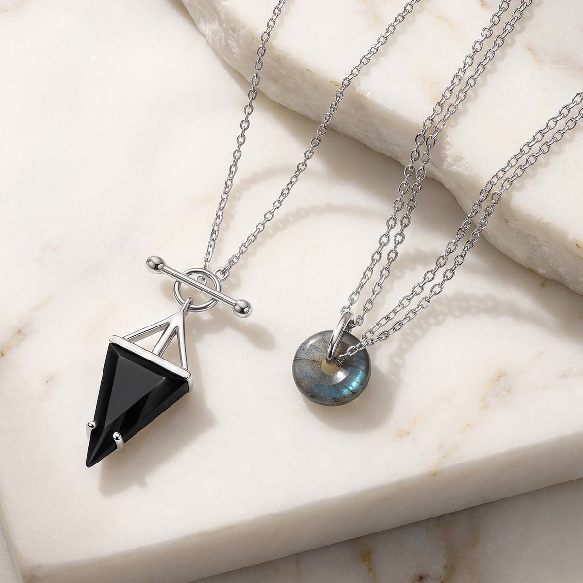 Silver necklaces on a marble surface with a black obsidian pendant and a labradorite donut