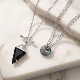 Silver necklaces on a marble surface with a black obsidian pendant and a labradorite donut