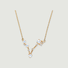 A yellow gold necklace with pale round moonstones and small clear stones forms an asymmetric V on a light grey background.