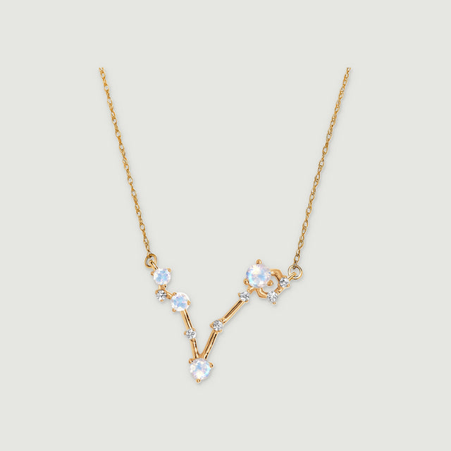 A yellow gold necklace with pale round moonstones and small clear stones forms an asymmetric V on a light grey background.