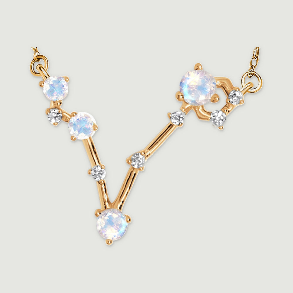 The complete V-shaped gold pendant lies against a light grey surface with both chain attachments visible.