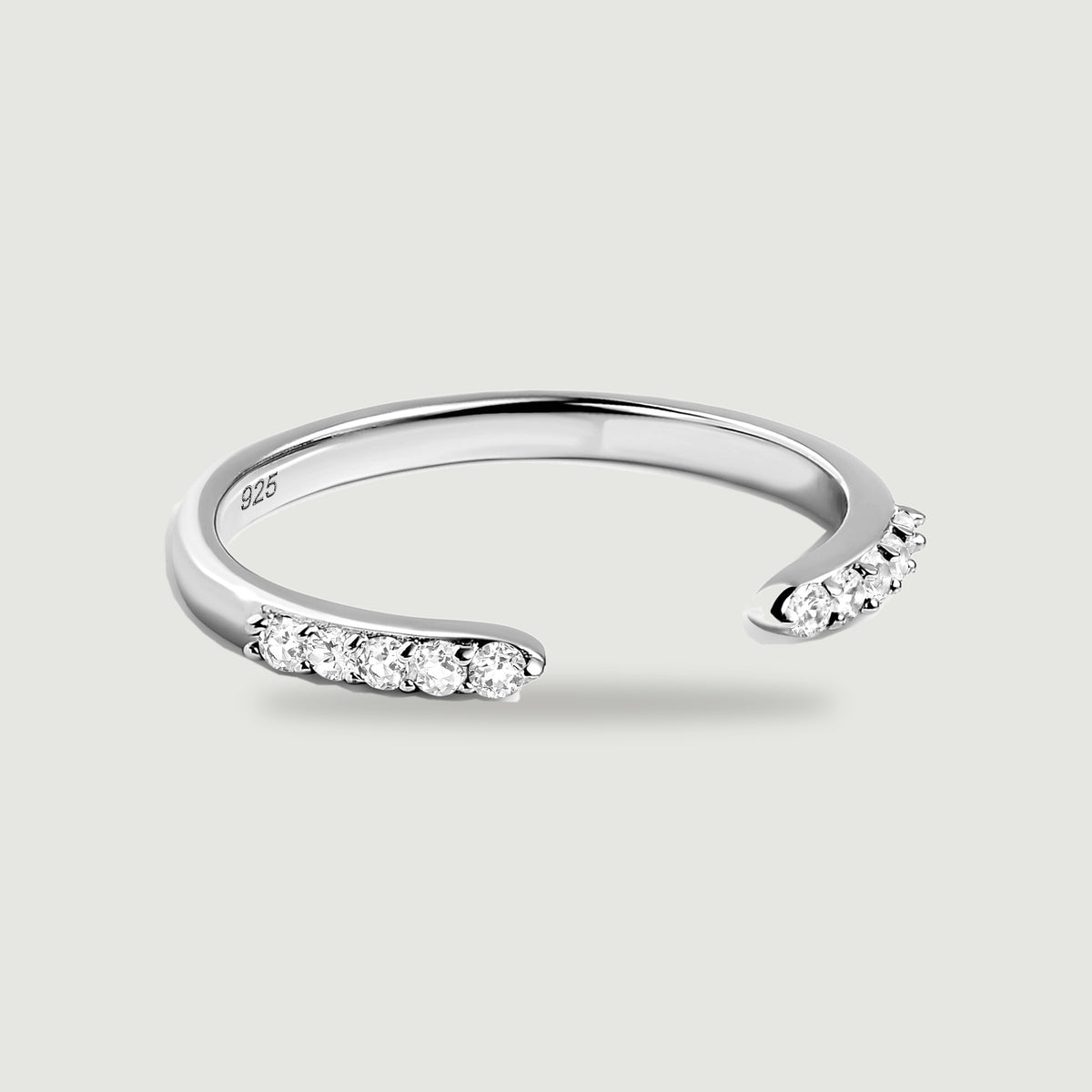 A silver open band has two rows of clear round stones facing each other on a light gray surface.