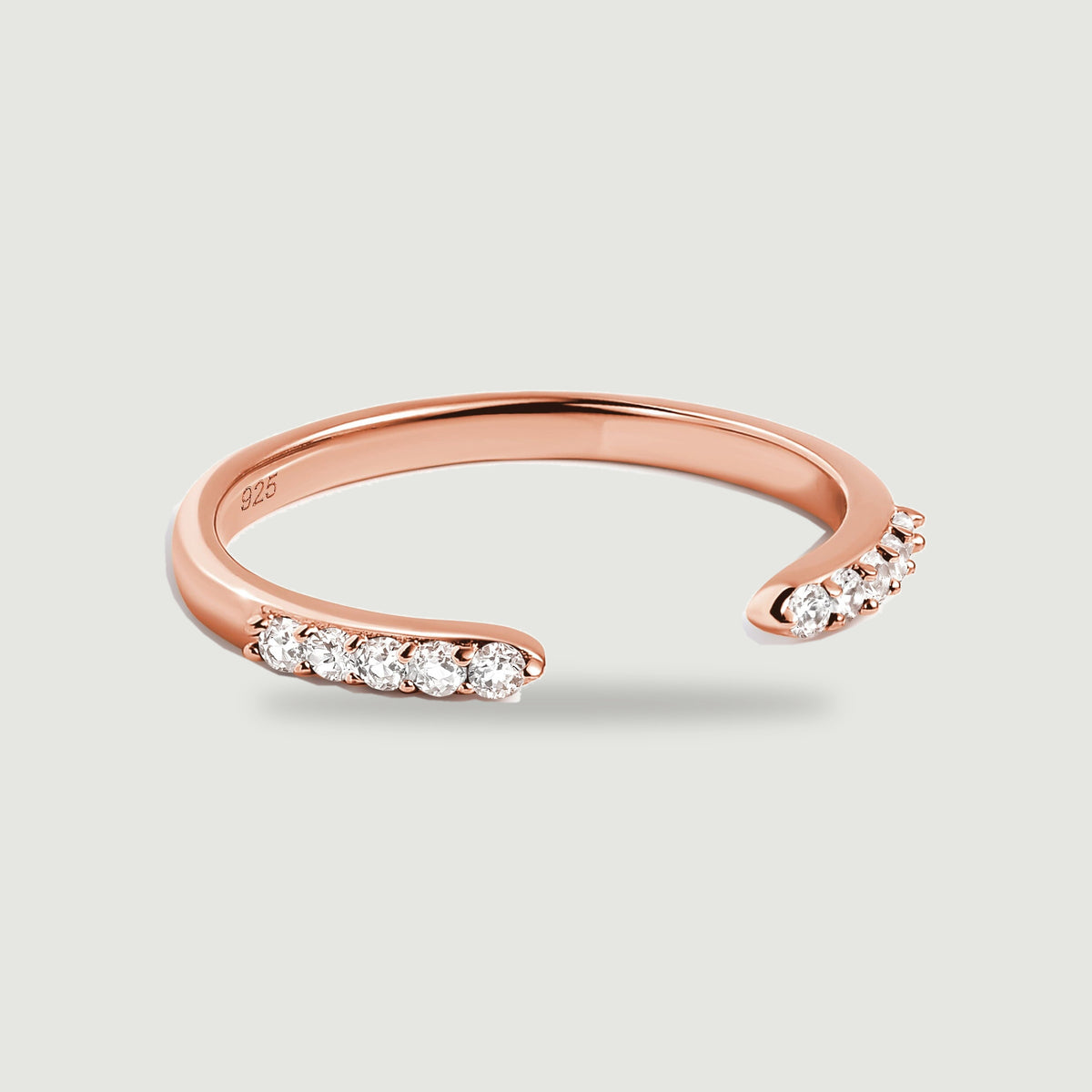 A rose gold open band rests on pale gray with clear stones lining its curved ends.