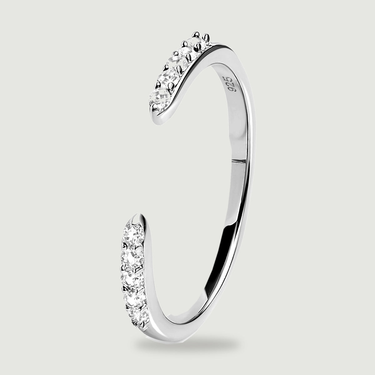 An upright silver ring reveals its slim curved profile and clear stones beside the open gap.
