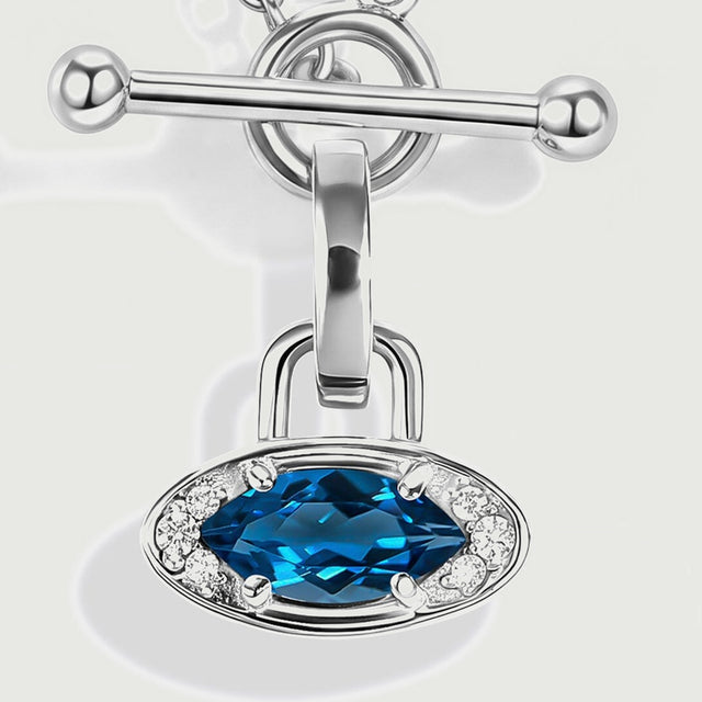 A front close-up highlights the oval blue gemstone, four silver prongs, clear accent stones and the hanging clasp connection.