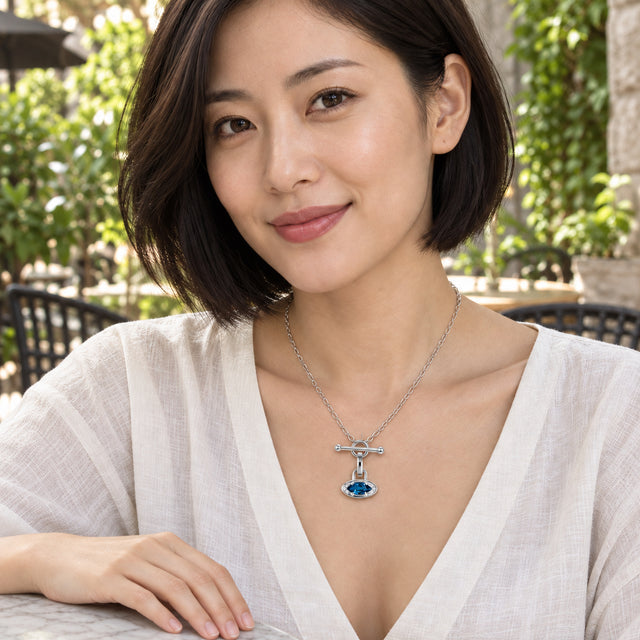 A woman with a dark bob wears a silver necklace with a blue pendant while seated at a leafy cafe table.
