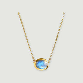 A round blue-flashing moonstone sits in a yellow gold bezel between two fine chains on a pale gray background.