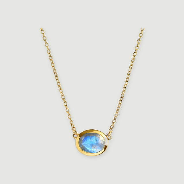 A round blue-flashing moonstone sits in a yellow gold bezel between two fine chains on a pale gray background.