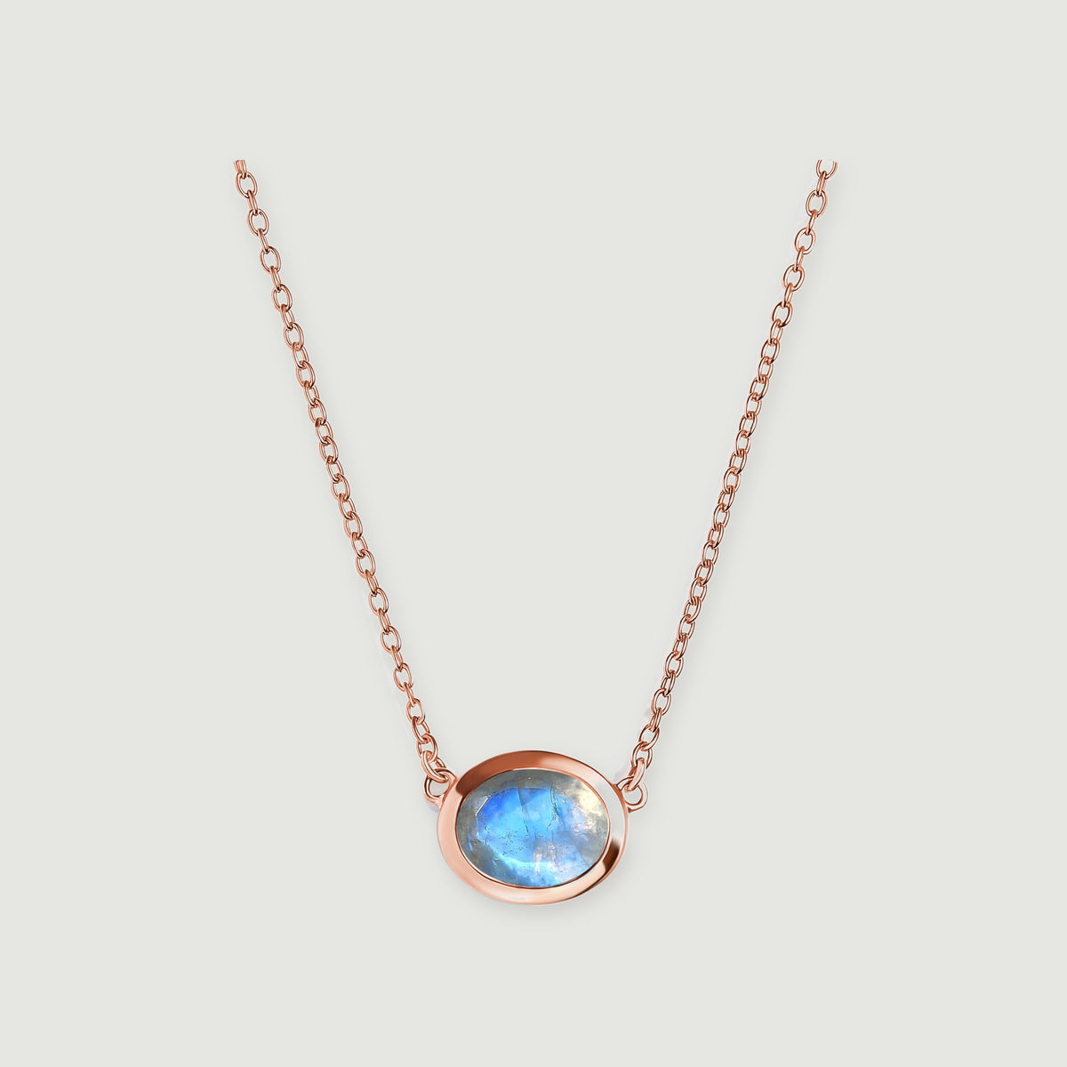 A rose gold necklace frames a translucent moonstone with a bright blue reflection.
