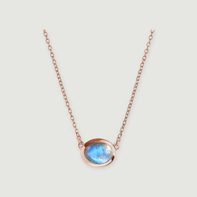 A rose gold necklace frames a translucent moonstone with a bright blue reflection.