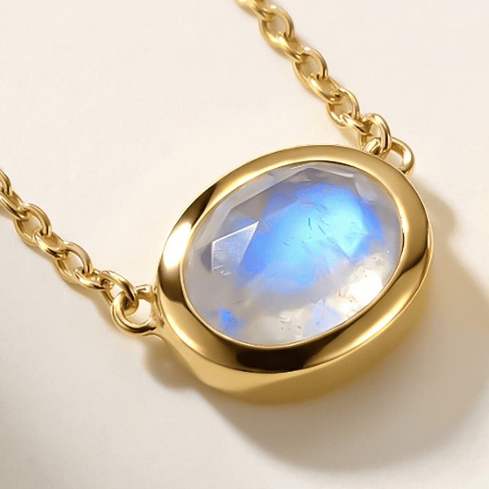 The faceted moonstone and rounded yellow gold rim appear close up on a clean pale surface.