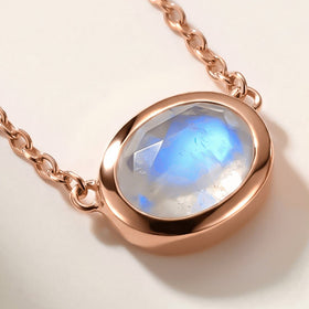A rose gold moonstone necklace rests flat on a pale tabletop with its fine chain extending to the edges.