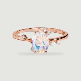 An oval moonstone and six small round diamonds sit on a polished rose gold ring.
