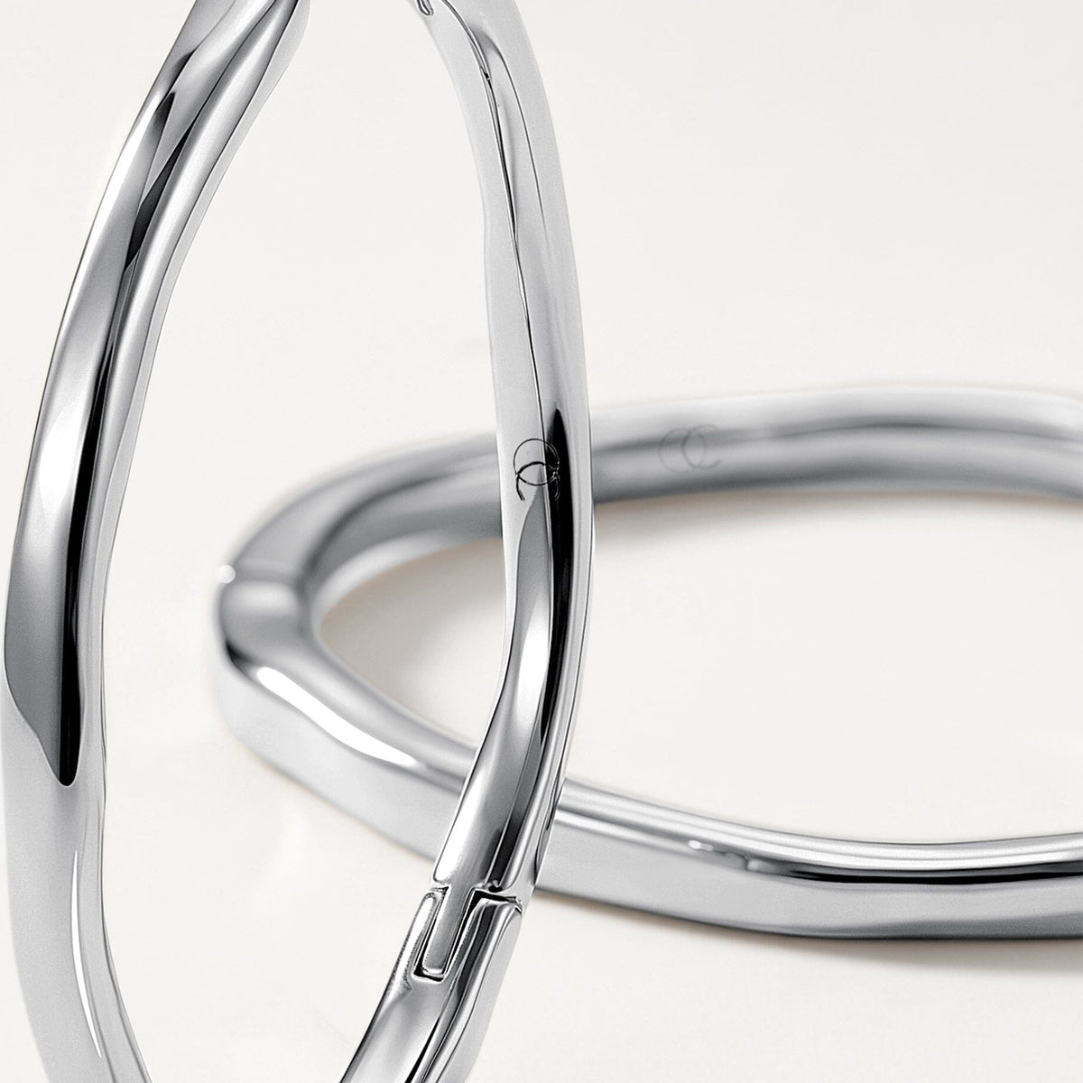 Macro product view shows two polished elongated hoops overlapping on a bright white surface.