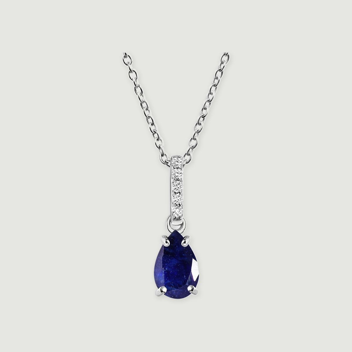 A silver cable chain holds a deep blue pear-shaped sapphire and a stone-set bail.