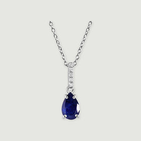 A silver cable chain holds a deep blue pear-shaped sapphire and a stone-set bail.